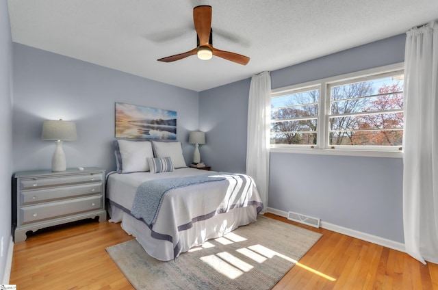 bedroom featuring ceiling fan, visible vents, baseboards, and wood finished floors