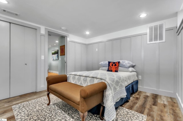 bedroom featuring a decorative wall, wood finished floors, visible vents, and multiple closets