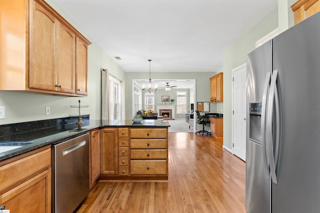kitchen featuring a peninsula, a warm lit fireplace, stainless steel appliances, light wood-style floors, and open floor plan