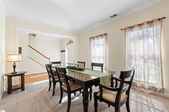 dining area featuring visible vents, light colored carpet, stairway, and crown molding