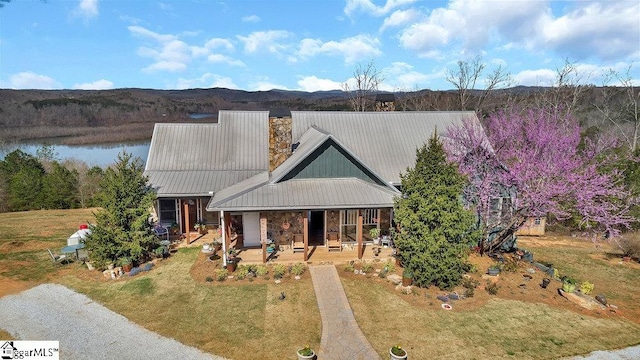 view of front of property with a front yard, covered porch, a chimney, a water view, and metal roof