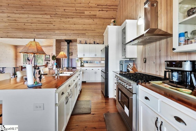 kitchen with extractor fan, freestanding refrigerator, stainless steel range, wood counters, and a kitchen island with sink