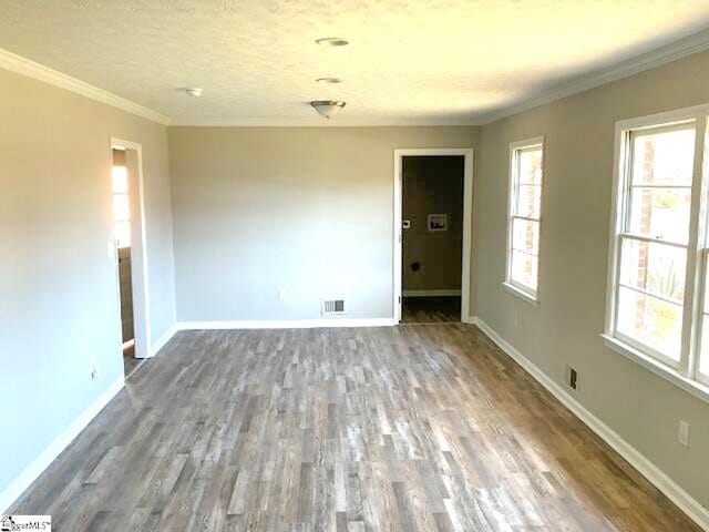 empty room featuring wood finished floors, crown molding, baseboards, and visible vents