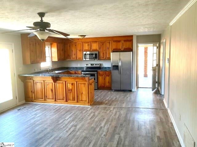 kitchen featuring light wood finished floors, a peninsula, brown cabinets, stainless steel appliances, and ceiling fan