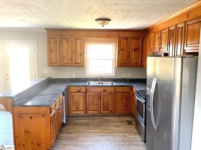 kitchen with a peninsula, dark countertops, stainless steel appliances, a sink, and brown cabinetry