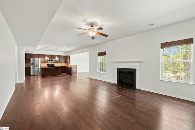 unfurnished living room featuring dark wood-type flooring, visible vents, baseboards, and ceiling fan