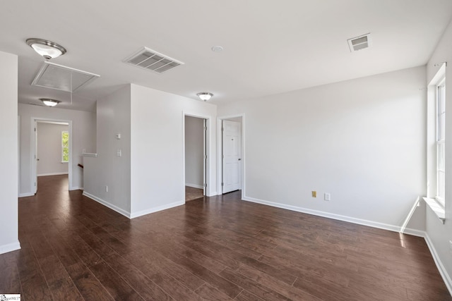 unfurnished room featuring dark wood-style flooring, visible vents, baseboards, and attic access