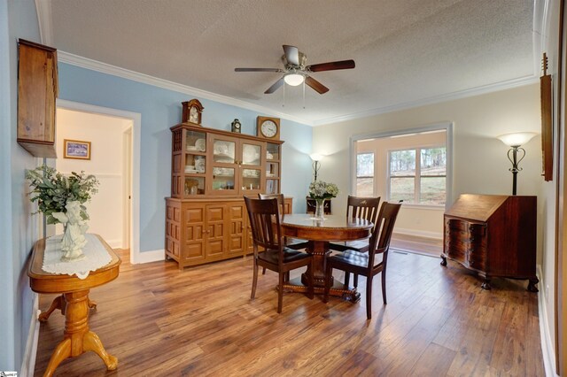 dining area featuring a textured ceiling, baseboards, ornamental molding, wood finished floors, and a ceiling fan