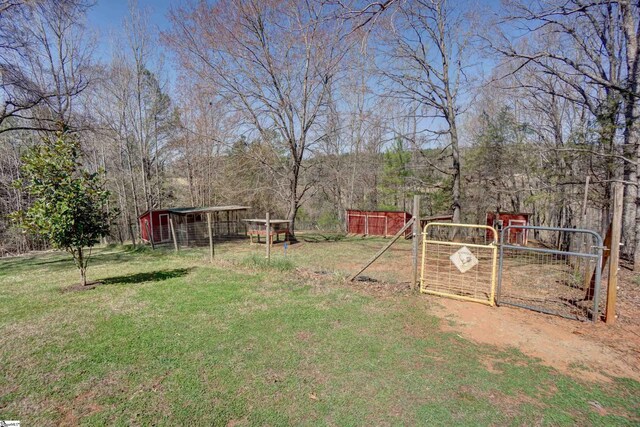 view of yard featuring an outdoor structure, a detached carport, a gate, and fence