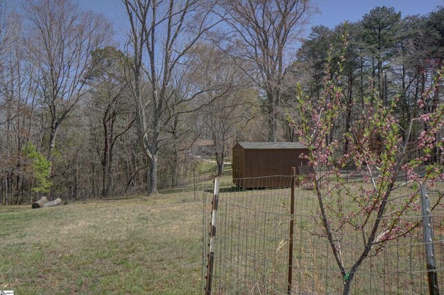 view of yard featuring a wooded view, an outbuilding, fence, and a storage unit