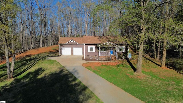 view of front facade with a view of trees, a front yard, an attached garage, and concrete driveway