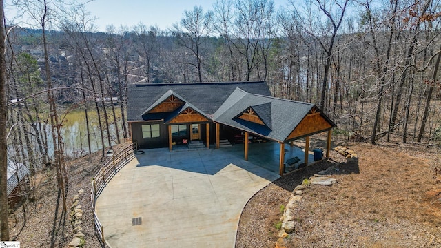 rustic home featuring a view of trees and roof with shingles