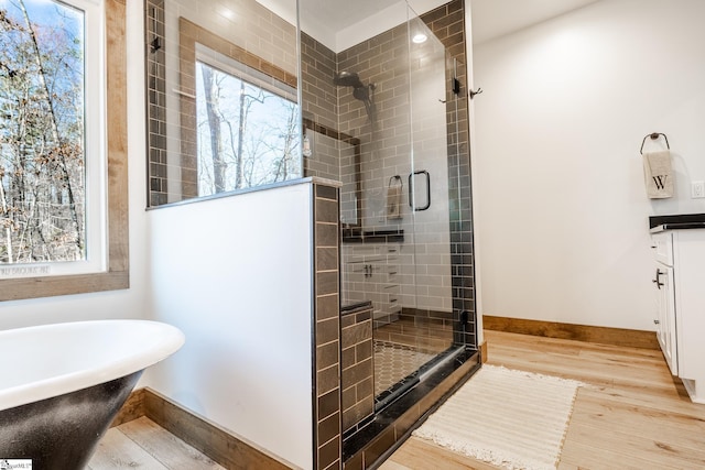 bathroom featuring baseboards, wood finished floors, a stall shower, and a soaking tub