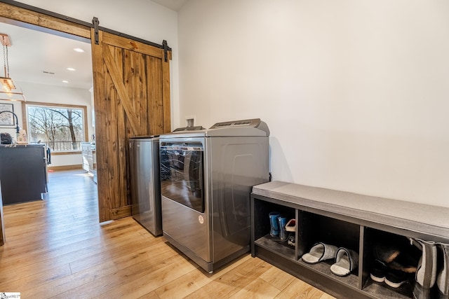 laundry area with washing machine and dryer, laundry area, a barn door, and light wood finished floors