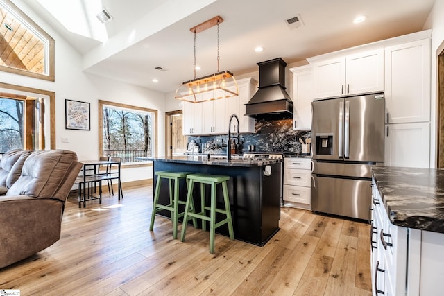 kitchen featuring stainless steel fridge, a breakfast bar, premium range hood, tasteful backsplash, and open floor plan