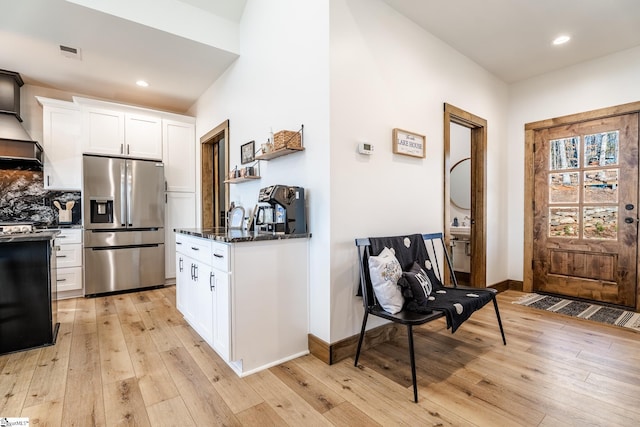 kitchen with white cabinetry, light wood-type flooring, stainless steel refrigerator with ice dispenser, visible vents, and decorative backsplash