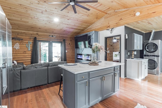 kitchen with stacked washer and dryer, gray cabinets, open floor plan, rustic walls, and ceiling fan
