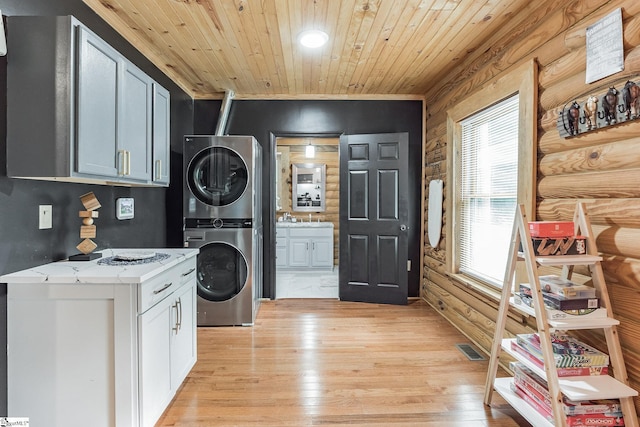 laundry area with light wood-style flooring, stacked washer / dryer, log walls, laundry area, and wooden ceiling