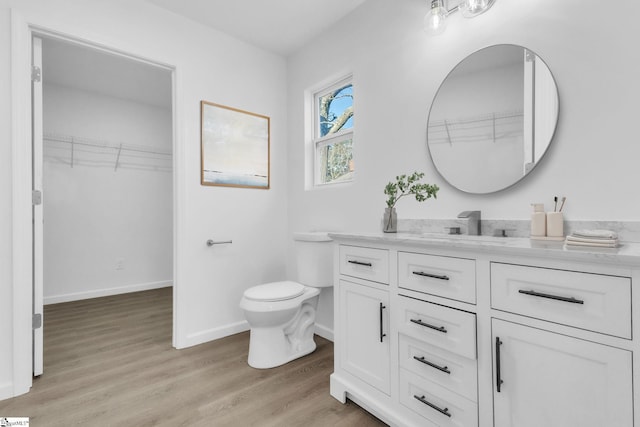 bathroom featuring a walk in closet, wood finished floors, vanity, baseboards, and toilet