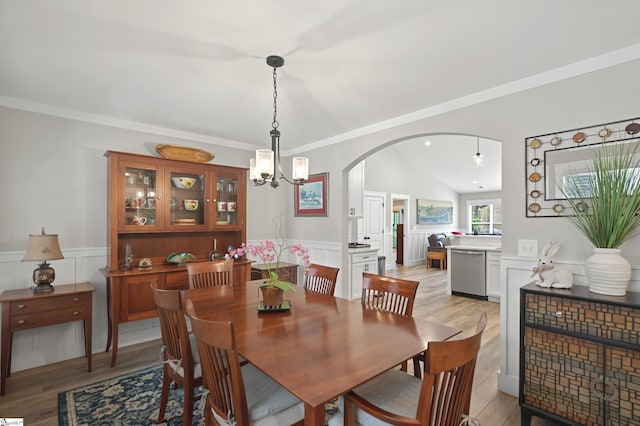 dining space with ornamental molding, arched walkways, light wood-style floors, and wainscoting