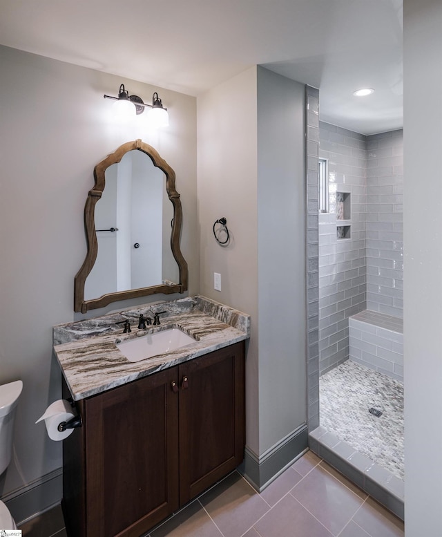 bathroom with tile patterned floors, toilet, tiled shower, vanity, and baseboards