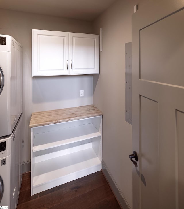 laundry area featuring stacked washer / dryer, electric panel, baseboards, cabinet space, and dark wood-style floors