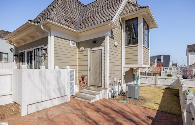 view of exterior entry with central air condition unit, a gate, fence, and a patio