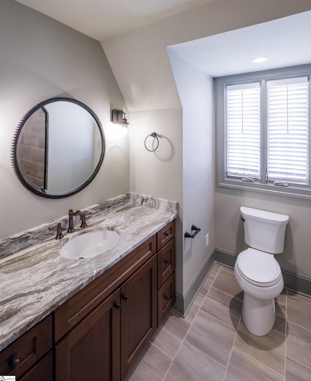 bathroom featuring toilet, vanity, baseboards, and vaulted ceiling