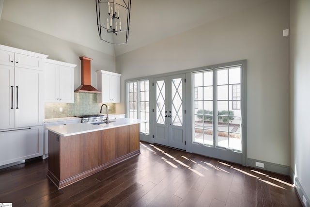 kitchen featuring light countertops, a sink, a center island with sink, wall chimney range hood, and dark wood-style flooring