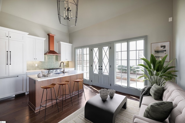 kitchen featuring light countertops, a kitchen island with sink, wall chimney exhaust hood, white cabinetry, and dark wood-style floors