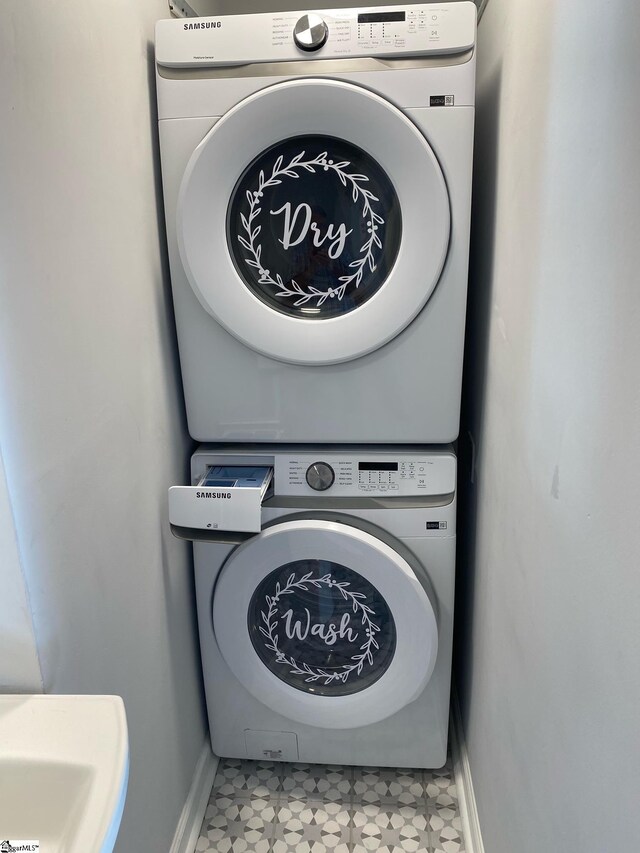 laundry area with baseboards, stacked washer / dryer, tile patterned floors, and laundry area