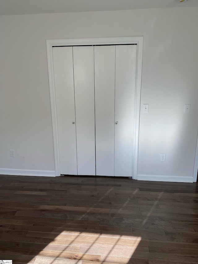 unfurnished bedroom featuring a closet, dark wood-style flooring, and baseboards