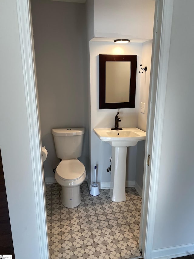 half bath with toilet, a sink, tile patterned floors, and baseboards