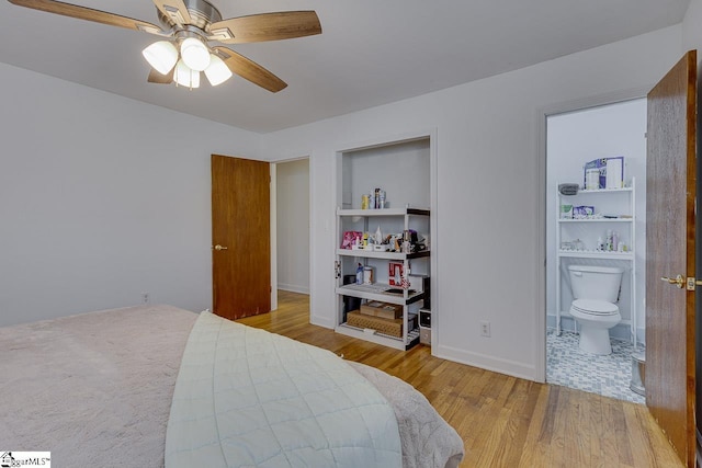 bedroom with baseboards, wood finished floors, ensuite bath, and a ceiling fan
