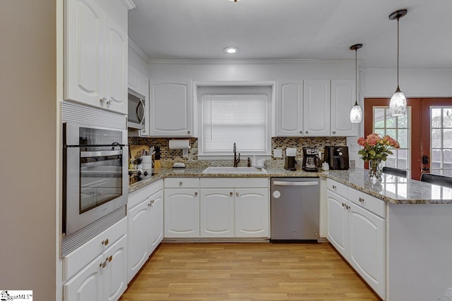 kitchen featuring stainless steel appliances, a sink, light wood-style floors, white cabinets, and a peninsula