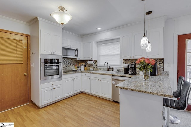 kitchen with a sink, appliances with stainless steel finishes, a peninsula, white cabinets, and light wood-style floors