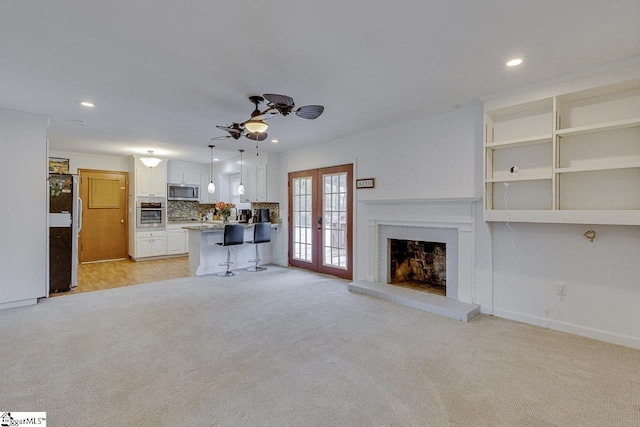 unfurnished living room featuring french doors, a ceiling fan, light carpet, a brick fireplace, and recessed lighting