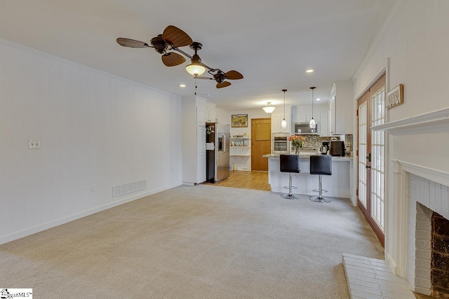 living area featuring a ceiling fan, a brick fireplace, light colored carpet, visible vents, and ornamental molding
