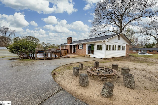 view of front facade featuring curved driveway, an outdoor fire pit, a chimney, a wooden deck, and brick siding
