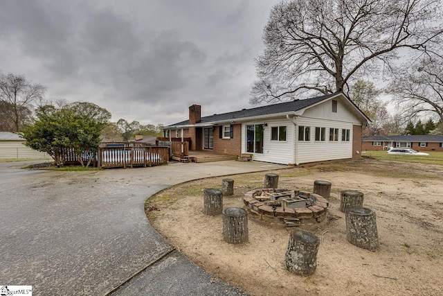 rear view of property with a wooden deck, driveway, an outdoor fire pit, brick siding, and a chimney