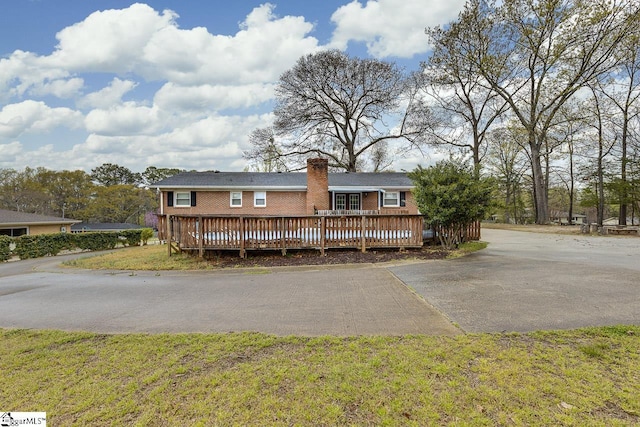 view of front of house featuring aphalt driveway, a deck, a front yard, brick siding, and a chimney
