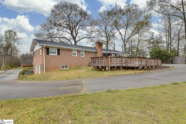 exterior space with a wooden deck, a storage shed, brick siding, a front lawn, and an outdoor structure