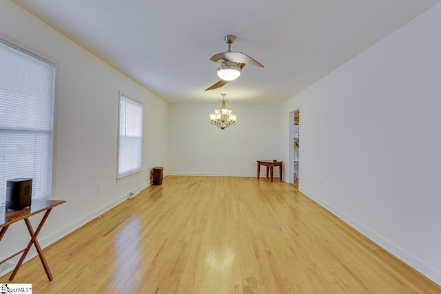 spare room featuring light wood-style flooring, ceiling fan with notable chandelier, baseboards, and visible vents