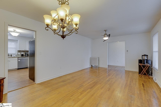empty room with a sink, ceiling fan with notable chandelier, baseboards, and light wood-type flooring