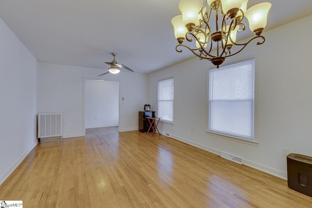 empty room featuring light wood-style flooring, visible vents, and ceiling fan with notable chandelier
