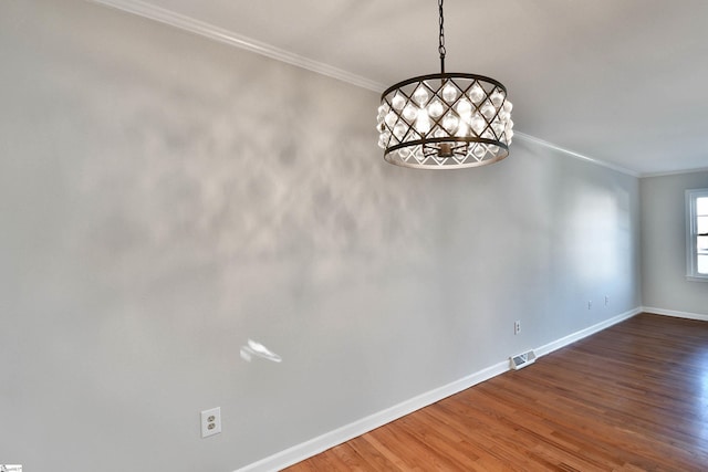 empty room with visible vents, baseboards, ornamental molding, wood finished floors, and a notable chandelier