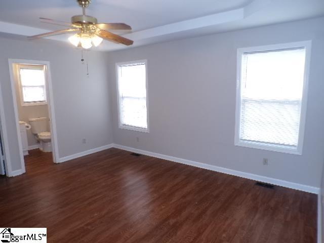 unfurnished bedroom featuring ensuite bathroom, dark wood-style floors, and baseboards