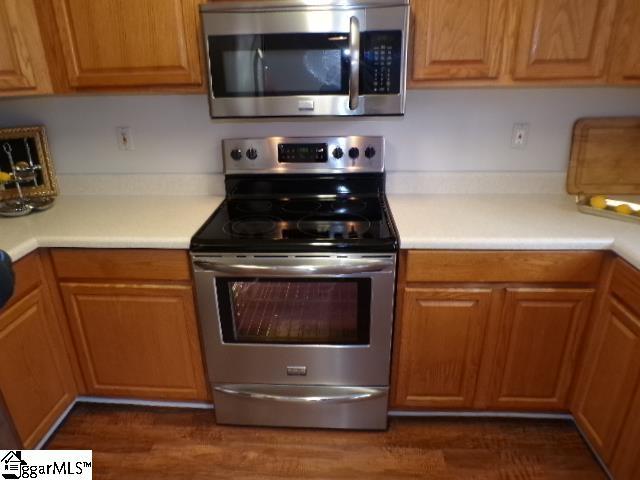kitchen with light countertops, appliances with stainless steel finishes, brown cabinets, and dark wood finished floors