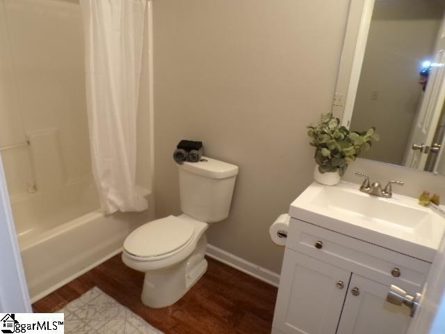 bathroom featuring vanity, shower / bathtub combination with curtain, toilet, baseboards, and wood finished floors