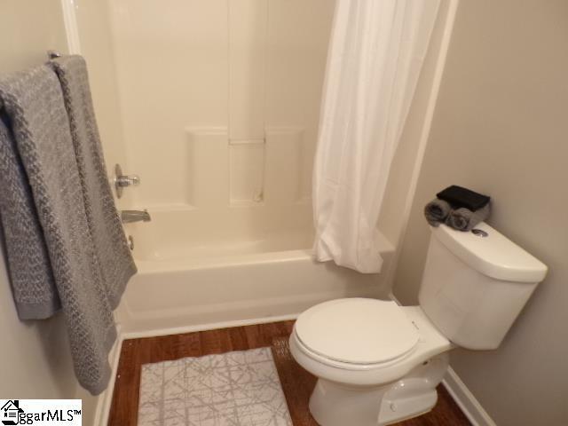 bathroom with toilet, shower / bath combo with shower curtain, and wood finished floors